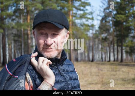 Un homme d'âge moyen dans un chapeau, souriant, marche dans le parc. Une journée ensoleillée. Bonne humeur. Banque D'Images