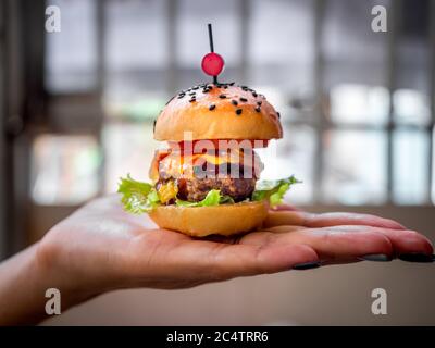 Hamburger maison prêt à manger. Mini-hamburger juteux maison avec bœuf, fromage, tomates fraîches en tranches, laitue verte et oignons caramélisés à la main. Banque D'Images