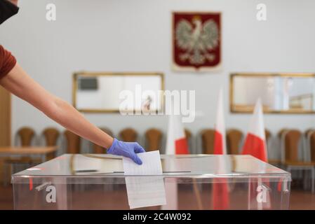 Femme avec masque et gants, en raison de la pandémie Covid-19, jetant une carte avec un vote aux urnes pendant les élections. Dans le vernis à l'arrière Banque D'Images