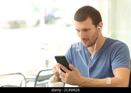 Homme avec casque écoute de la musique sur un smartphone assis sur une terrasse de café Banque D'Images