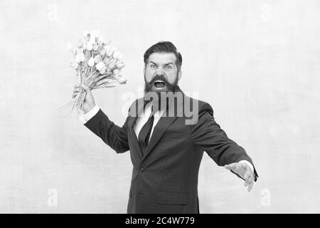 Des vacances de haine. Journée pour femme. 8 Mars. Homme barbu en colère avec des fleurs. Fêtez le printemps. Échec de la date. Irritée, l'homme barbu agacé avec bouquet de tulipes. Concept déçu. Date d'échec. Banque D'Images