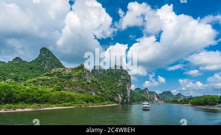 Vue panoramique du bateau touristique transportant des touristes naviguant parmi les hautes falaises verticales des montagnes karstiques sur la magnifique rivière Li qui coule entre Banque D'Images