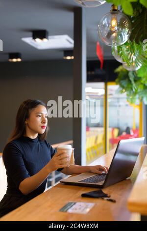 Jeune femme d'affaires asiatique magnifique utilisant un ordinateur portable et assis à distance à l'intérieur du café Banque D'Images