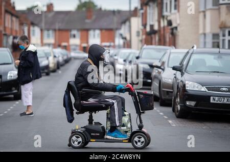 Un homme portant une visière protectrice traverse la route sur un scooter de mobilité à Leicester car la ville peut être le premier site britannique à être soumis à un verrouillage local après une pointe dans les cas de coronavirus. Banque D'Images