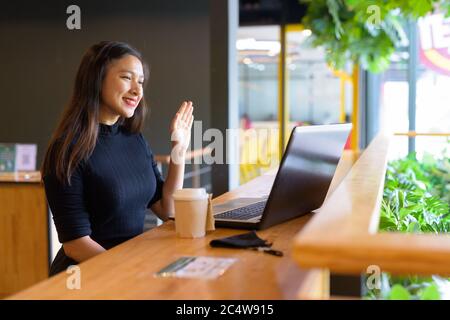 Joyeux jeune femme d'affaires asiatique belle appels vidéo tout en étant assis à distance dans le café Banque D'Images