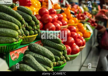 Beaucoup de tomates se trouvent l'une sur l'autre en forme de pyramide dans la lumière du soleil près des gros concombres verts Banque D'Images