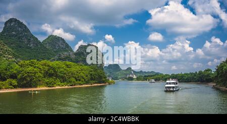 Vue panoramique du bateau touristique transportant des touristes naviguant parmi les hautes falaises verticales des montagnes karstiques sur la magnifique rivière Li qui coule entre Banque D'Images