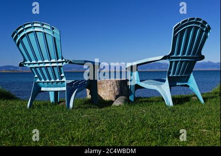 Deux chaises bleues sont sur l'herbe donnant sur la mer et les montagnes au-delà. Un souche d'arbre est utilisé comme table Banque D'Images