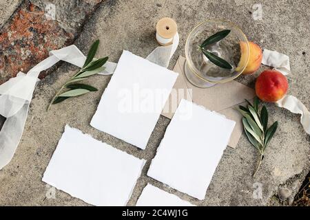 Papeterie de mariage d'été, scène de vie. Cartes vierges, jeux de maquettes d'invitations. Branches d'olive, ruban de soie, pêches, fruits et champagne Banque D'Images