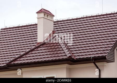 un toit brun d'un carrelage en céramique avec un tuyau un système de drainage et un tuyau d'évent, gros plan sur la structure architecturale d'une maison. Banque D'Images