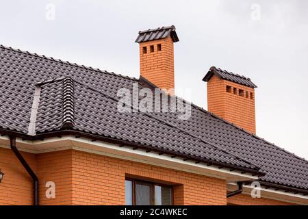 un toit brun d'un carrelage en céramique avec un tuyau un système de drainage de tempête, gros plan des détails de la structure architecturale de la maison de brique. Banque D'Images