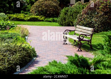 Banc rétro en bois avec pieds forgés montés dans le parc avec des plantes et des buissons vue latérale, personne. Banque D'Images