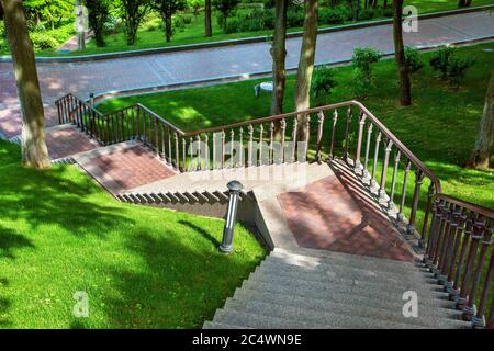 escaliers en pierre avec dalles de pavage et mains courantes en fer descendant jusqu'au chemin pour marcher dans le parc parmi les arbres et les pelouses vertes Banque D'Images