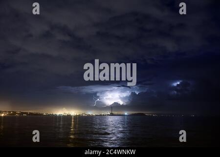 La nuit, la foudre surfait la mer ou le lac. Orage au-dessus de la grande ville industrielle. Banque D'Images