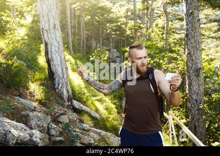 Homme de randonnée élégant barbu utilisant la navigation gps pour se positionner sur le sentier de montagne et pense où aller. Concept de technologie Banque D'Images