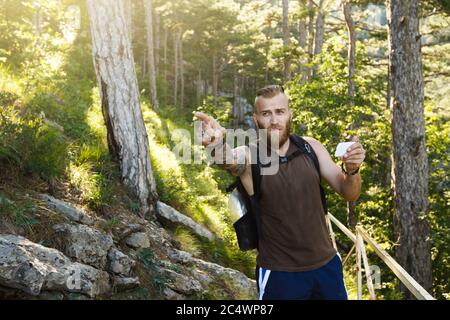 Homme de randonnée élégant barbu utilisant la navigation gps pour se positionner sur le sentier de montagne et pense où aller. Concept de technologie Banque D'Images