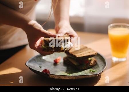 Femme tient dans les mains mordu sandwich. Pain grillé au seigle avec avocat. Jus d'orange frais nourriture végétarienne Banque D'Images