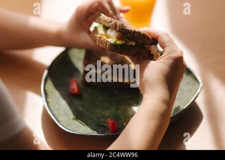 Femme tient dans les mains mordu sandwich. Pain grillé au seigle avec avocat. Jus d'orange frais nourriture végétarienne Banque D'Images