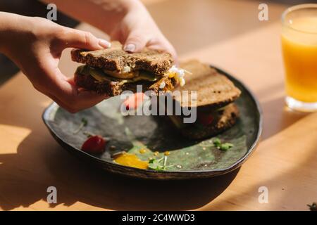 Femme tient dans les mains mordu sandwich. Pain grillé au seigle avec avocat. Jus d'orange frais nourriture végétarienne Banque D'Images