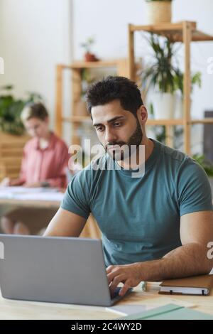 Portrait vertical d'un beau barbu à l'aide d'un ordinateur portable tout en travaillant sur un bureau en bois dans un bureau, espace de copie Banque D'Images