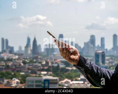 Un homme compose un message sur un smartphone sur le fond du panorama de la ville de Jakarta. Vidéo accélérée. Banque D'Images