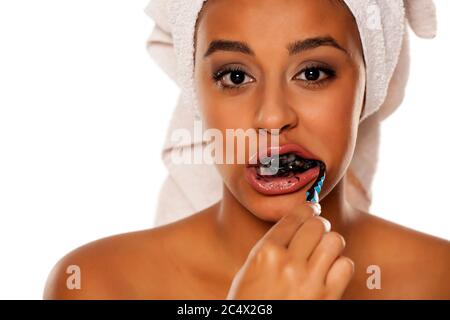 portrait d'une jeune femme à peau foncée se brossant les dents avec du dentifrice noir sur fond blanc Banque D'Images