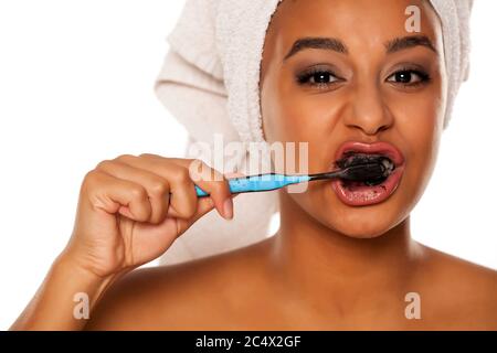 portrait d'une jeune femme heureuse à peau foncée se brossant les dents avec du dentifrice noir sur fond blanc Banque D'Images