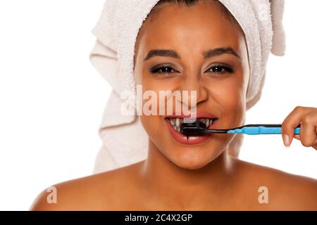 portrait d'une jeune femme heureuse à peau foncée se brossant les dents avec du dentifrice noir sur fond blanc Banque D'Images