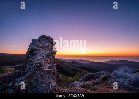 Coucher de soleil derrière un vieux mur en pierre qui donne sur la côte nord-ouest de la Corse et la mer Méditerranée avec la côte de la France continentale en t Banque D'Images