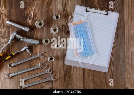 Mise en place de la spirale bloc-notes d'outils pour mécanicien d'auto, gants de travail dans clé à ergots automobile COVID-19 crise pandémique masque médical sur fond de bois Banque D'Images