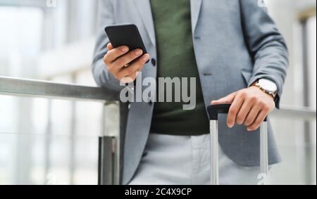 Homme d'affaires méconnu avec des bagages en voyage d'affaires, en utilisant un smartphone. Banque D'Images