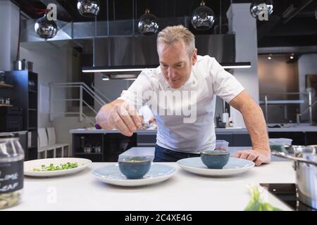 Chef de cuisine senior ajoutant du sel dans un plat dans la cuisine du restaurant Banque D'Images