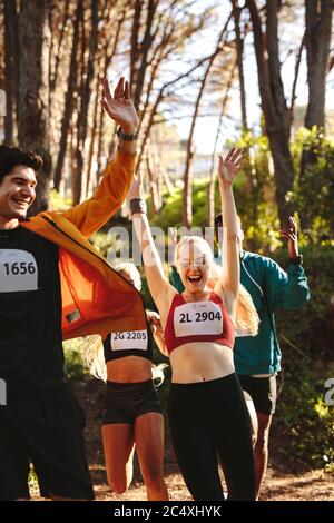 Groupe d'hommes et de femmes célébrant après avoir terminé la course en forêt. Les athlètes professionnels enthousiastes après avoir gagné la course. Banque D'Images