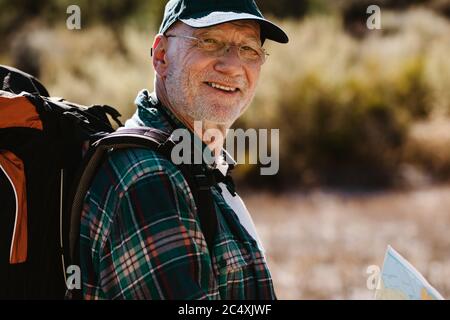 Homme âgé portant un sac à dos, regardant l'appareil photo et souriant. Faites de la randonnée avec le vieil homme. Banque D'Images
