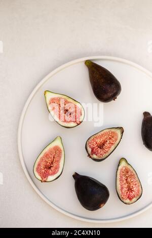 Image TopView de figues, entières et coupées en deux, dans une plaque ronde en céramique blanche sur fond gris clair. Espace négatif. Banque D'Images