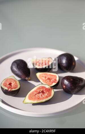 Image verticale des figues sur une plaque en céramique blanche filmée dans des conditions d'éclairage difficiles. Espace négatif. Banque D'Images