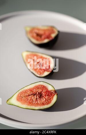 Image verticale des figues sur une plaque en céramique blanche filmée dans des conditions d'éclairage difficiles. Espace négatif. Banque D'Images