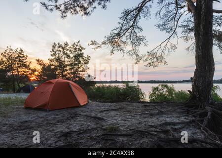 des tentes se dressent sur la rive de la rivière au lever du soleil Banque D'Images