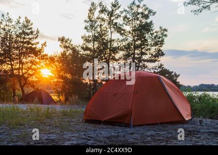 des tentes se dressent au lever du soleil sur la rive de la rivière Banque D'Images