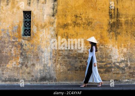 Fille vietnamienne en robe traditionnelle passant mur jaune Banque D'Images
