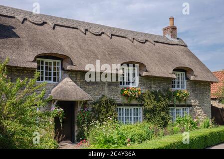 Maison pittoresque en pierre à toit de chaume à Thornton-le-Dale, dans le nord du Yorkshire. Un jardin de chalet est en premier plan et un ciel bleu avec des nuages au-dessus Banque D'Images