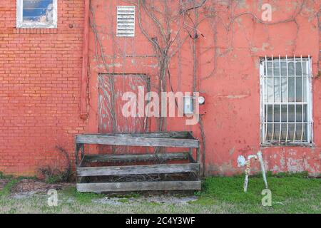 un bâtiment d'entrepôt abandonné avec une fenêtre barrée et une porte boartée avec de l'herbe Banque D'Images