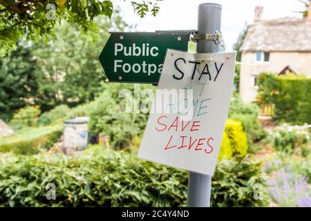 Restez à la maison, un avis de sauver des vies est lié à un panneau de sentier public pendant la pandémie Covid 19 dans le village de Cotswold, Sapperton, Gloucestershire, Royaume-Uni Banque D'Images