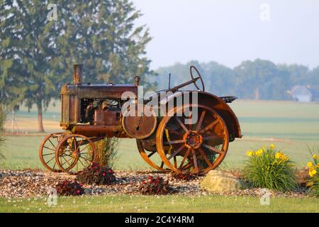 un tracteur de ferme d'époque rouillé exposé dans une ferme rurale aux fleurs vives tôt le matin Banque D'Images