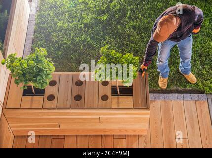 Charpentier mettant des touches de finition sur la table et le projet de terrasse en bois de création dans la zone résidentielle de cour arrière. Banque D'Images