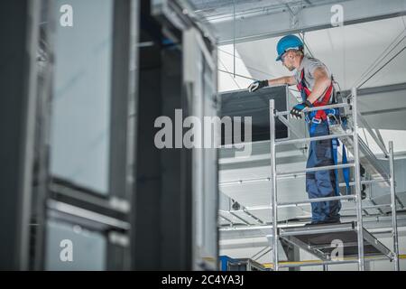 Ouvrier de construction vérifiant l'arbre de ventilation d'air nouvellement installé sur le plafond du grand bâtiment commercial. Banque D'Images