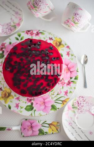Cheesecake à base de cassis dans un plat de fleurs. Cuillère, tasses pour thé et soucoupes sur une table blanche. Vue de dessus. Banque D'Images