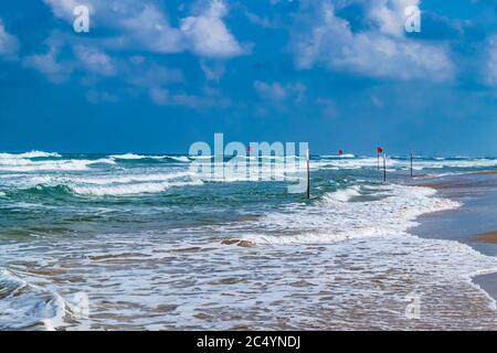 La natation est dangereuse dans les vagues. Drapeau rouge qui flotte dans le vent par temps de tempête sur la plage. Banque D'Images