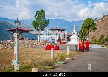 Jeunes femmes moines du monastère bouddhiste dans leurs robes rouges traditionnelles avant les classes à côté de la roue de prière sur le fond du Himal Banque D'Images