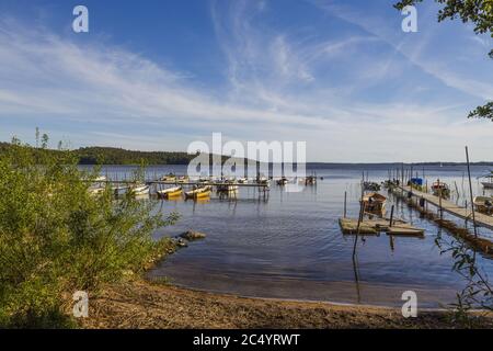 Belle nature vue sur le paysage aquatique le jour d'été. Parking bateaux en bois sur la côte du lac. Arbres verts et ciel bleu avec fond blanc de nuages. Suède Banque D'Images